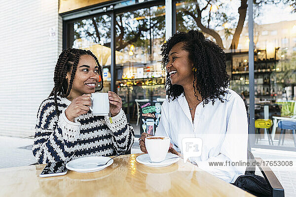 Happy businesswomen with coffee cups sitting at sidewalk cafe