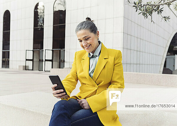 Happy businesswoman surfing net through smart phone sitting on bench