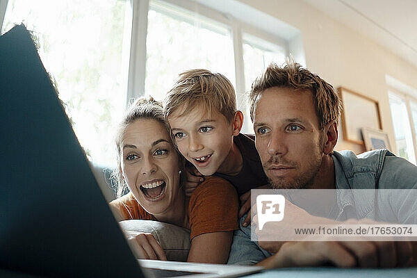 Glückliche Frau mit Sohn und Mann  die sich zu Hause Videos über den Laptop ansehen