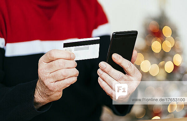 Hand of senior man holding credit card and mobile phone at home