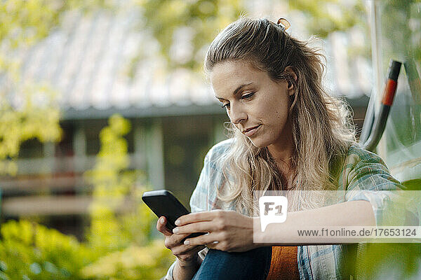 Blond woman text messaging through smart phone at backyard