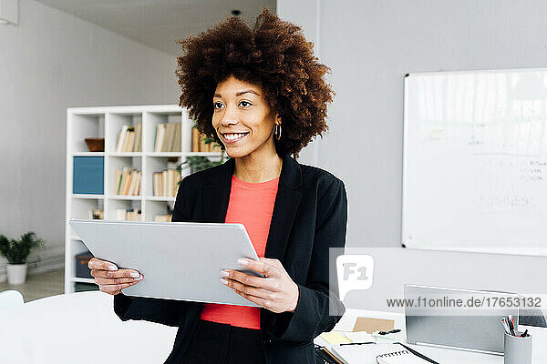 Smiling Afro businesswoman with tablet PC in office
