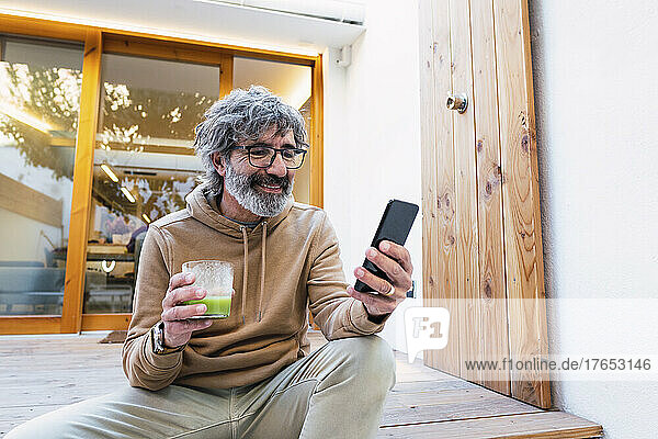 Smiling man with glass of smoothie sitting on patio