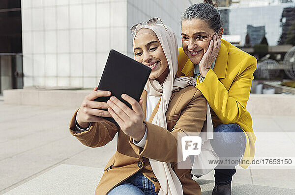 Lächelnde junge Geschäftsfrau  die im Büropark ein Selfie mit einem Kollegen über einen Tablet-PC macht