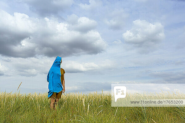 Woman standing amidst grass covered with blue scarf at meadow