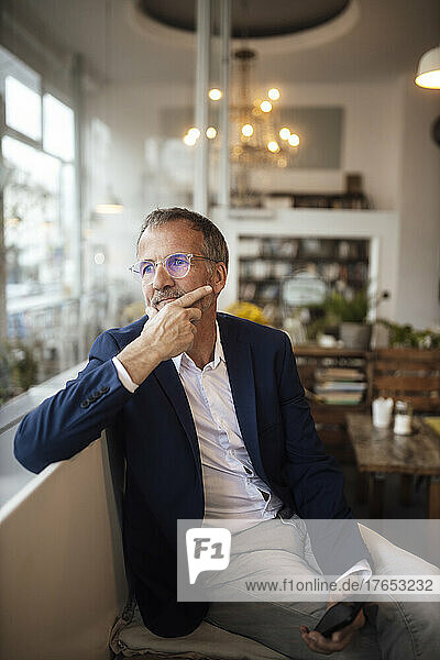 Thoughtful businessman with hand on chin sitting at cafe