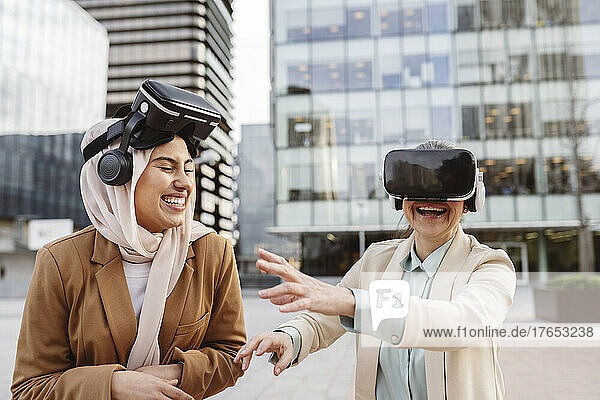 Cheerful businesswomen wearing virtual reality simulator enjoying outside modern building