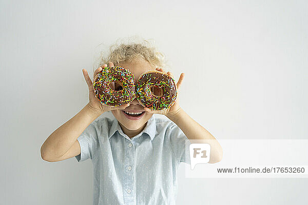 Glückliches Mädchen  das die Augen mit Donuts bedeckt  die vor der Wand stehen