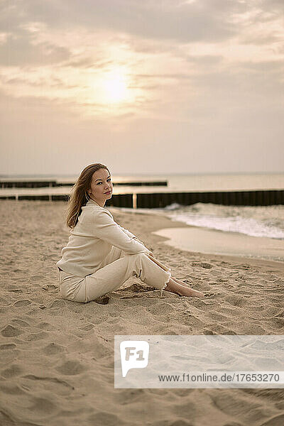 Schöne Frau sitzt bei Sonnenuntergang auf Sand