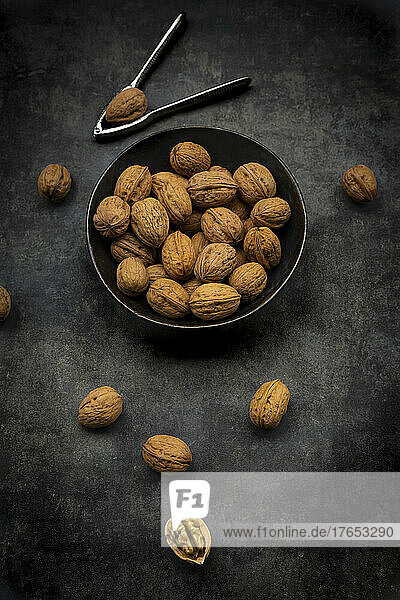 Studio shot of nutcracker and bowl of walnuts lying against black background