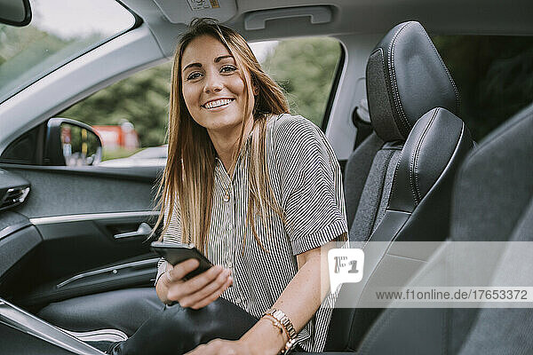 Happy blond woman with smart phone sitting on front passenger seat in car