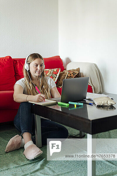 Young woman wearing headphones looking at laptop sitting in living room
