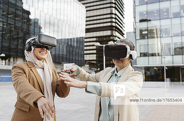 Lächelnde Geschäftskollegen mit Virtual-Reality-Simulator gestikulieren vor einem modernen Gebäude