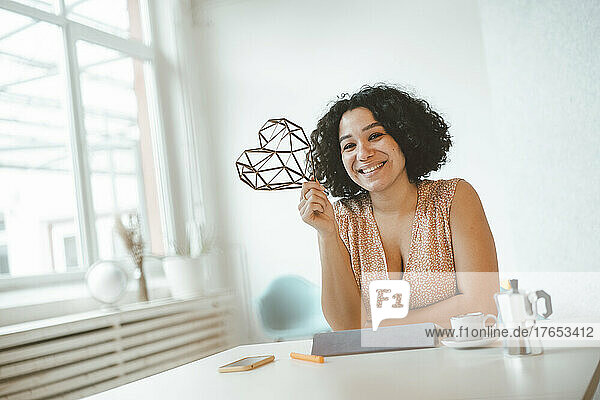 Happy freelancer with heart shaped object sitting at table
