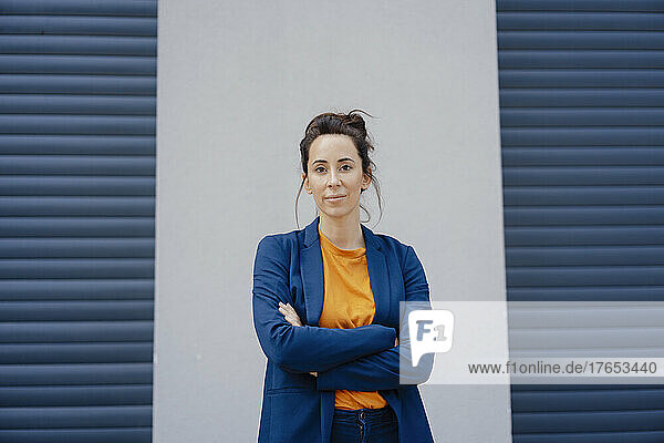 Businesswoman with arms crossed standing in front of gray wall