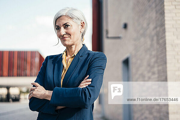 Smiling businesswoman standing with arms crossed on sunny day