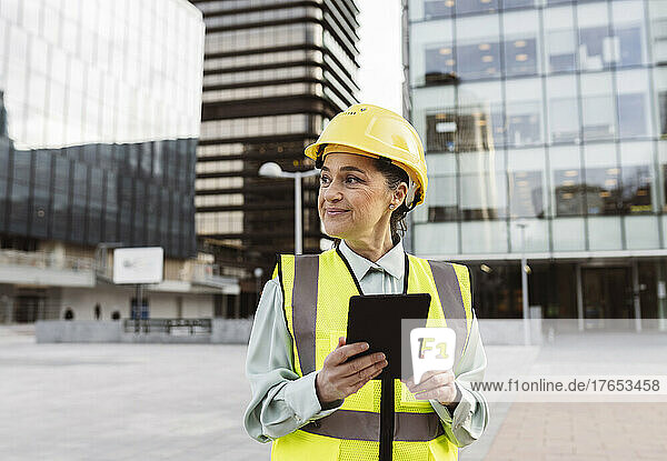 Smiling female architect with tablet PC standing outside building