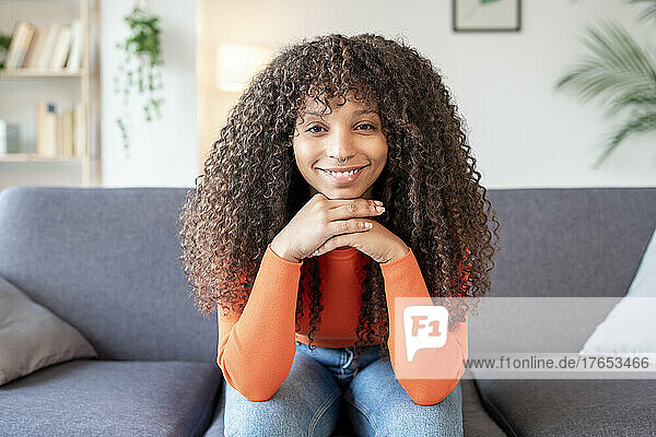Smiling young woman with curly hair sitting on sofa in living room