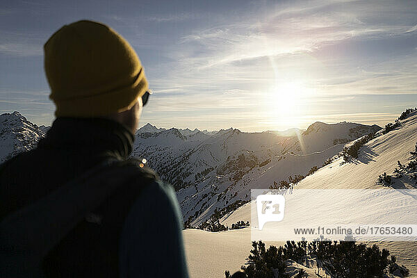 Mann mit Strickmütze genießt den Sonnenaufgang auf einem verschneiten Berg