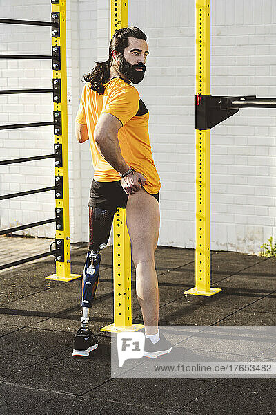 Amputated man with prosthetic leg standing in front of gymnastics bars