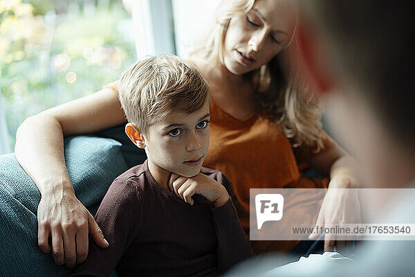 Blond boy sitting by mother looking at man on sofa at home