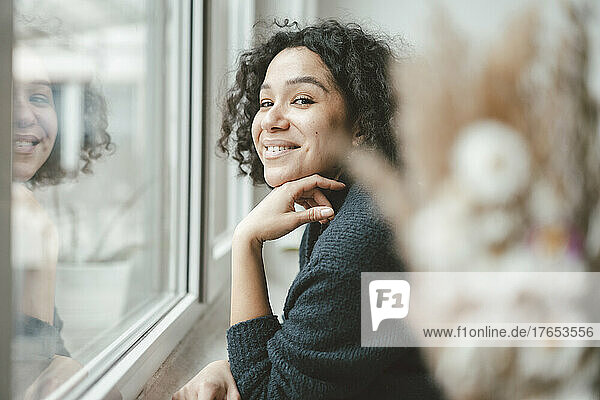 Happy beautiful woman standing by window at home