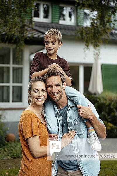 Smiling man carrying son on shoulders standing by man at backyard