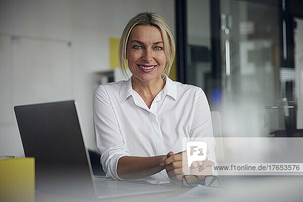 Smiling businesswoman with laptop at desk in office