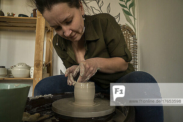 Woman making clay pot on pottery wheel at workshop