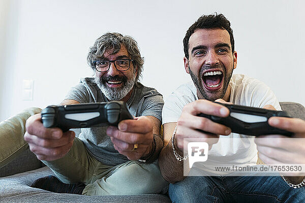 Cheerful father playing video game with son at home