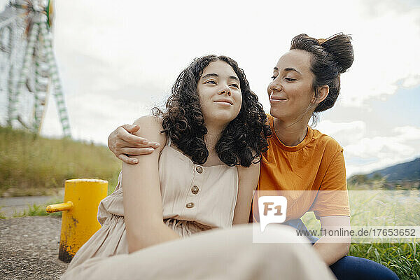 Smiling woman looking and embracing daughter sitting on roadside