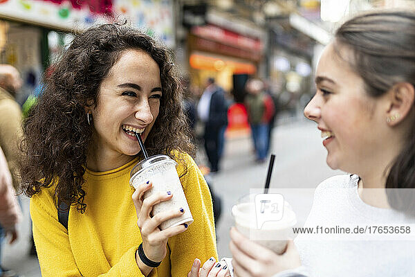 Happy young woman looking at friend drinking milkshake