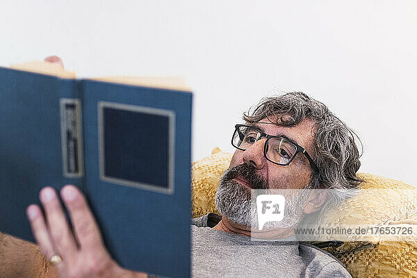 Senior man reading book by lying on sofa at home