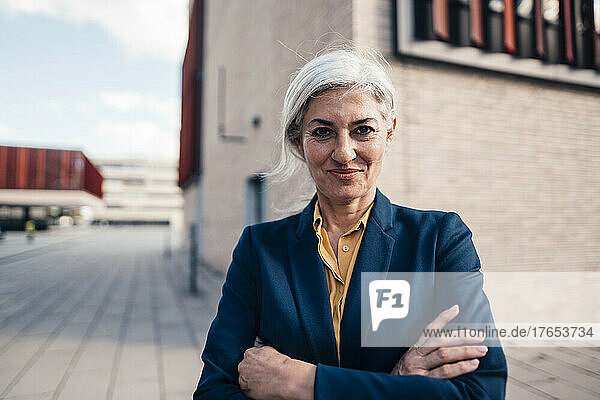 Smiling business person with arms crossed standing outside office building