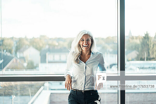 Happy woman with gray hair in front of glass window in office