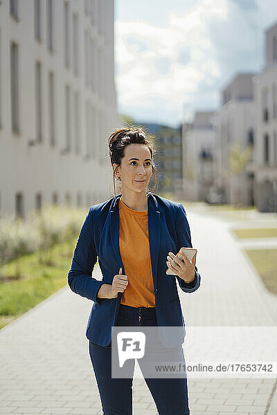 Businesswoman holding mobile phone standing on footpath