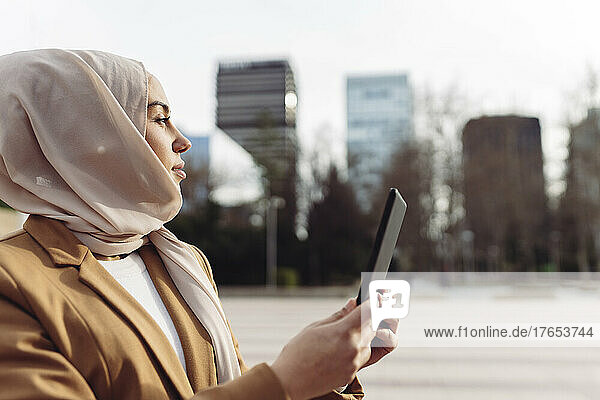 Businesswoman wearing hijab holding tablet PC on sunny day