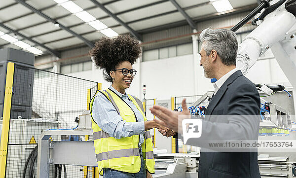 Smiling businessman gesturing and shaking hand with engineer in factory