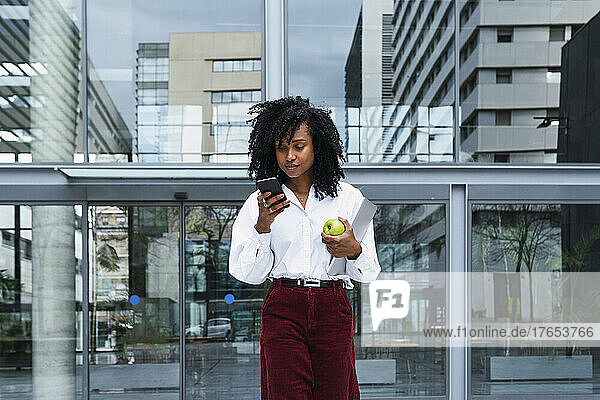 Businesswoman with curly hair using mobile phone at office park