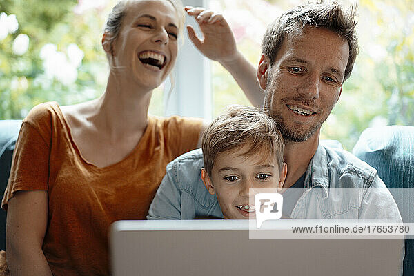 Cheerful woman sitting by man and son sharing laptop at home
