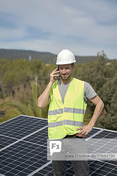 Engineer talking on mobile phone standing in front of solar panels on sunny day