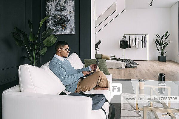 Freelancer wearing eyeglasses using laptop sitting on sofa at home
