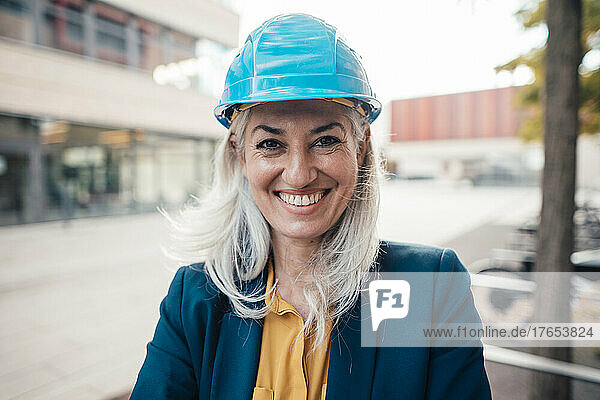 Happy female architect wearing hardhat standing at office park