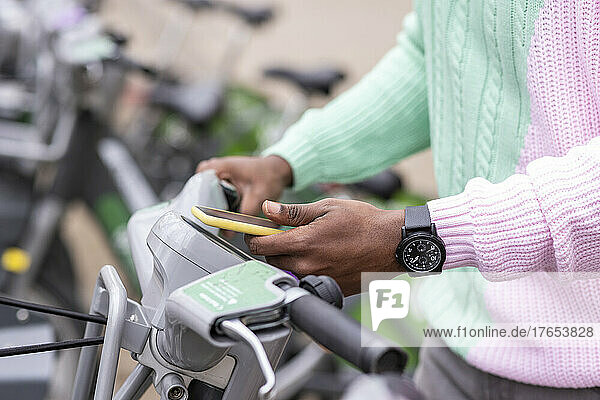 Hand eines Mannes  der am Parkplatz per Mobiltelefon ein Fahrrad mietet