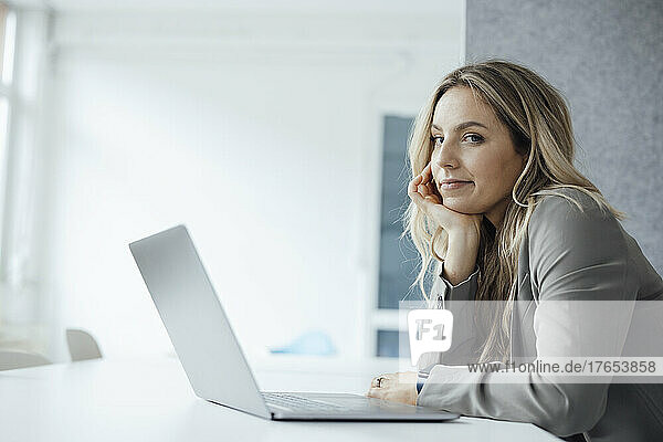 Frau mit Hand am Kinn und Laptop am Schreibtisch im Büro