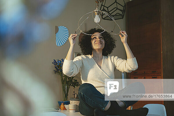 Smiling woman holding pendant light over head at home