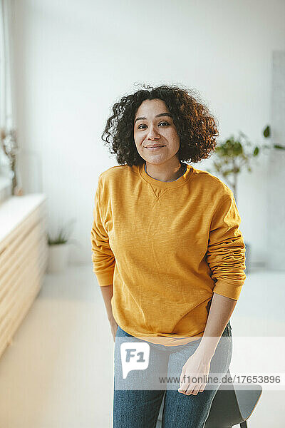 Smiling woman with curly hair leaning on chair at home