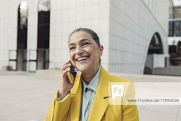 Glückliche Geschäftsfrau  die im Büropark mit dem Smartphone spricht