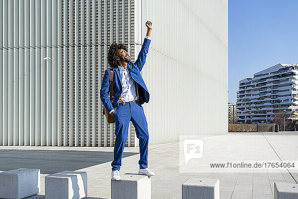Happy businessman standing with hand raised on concrete block