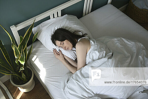 Woman with blanket sleeping in bed at home